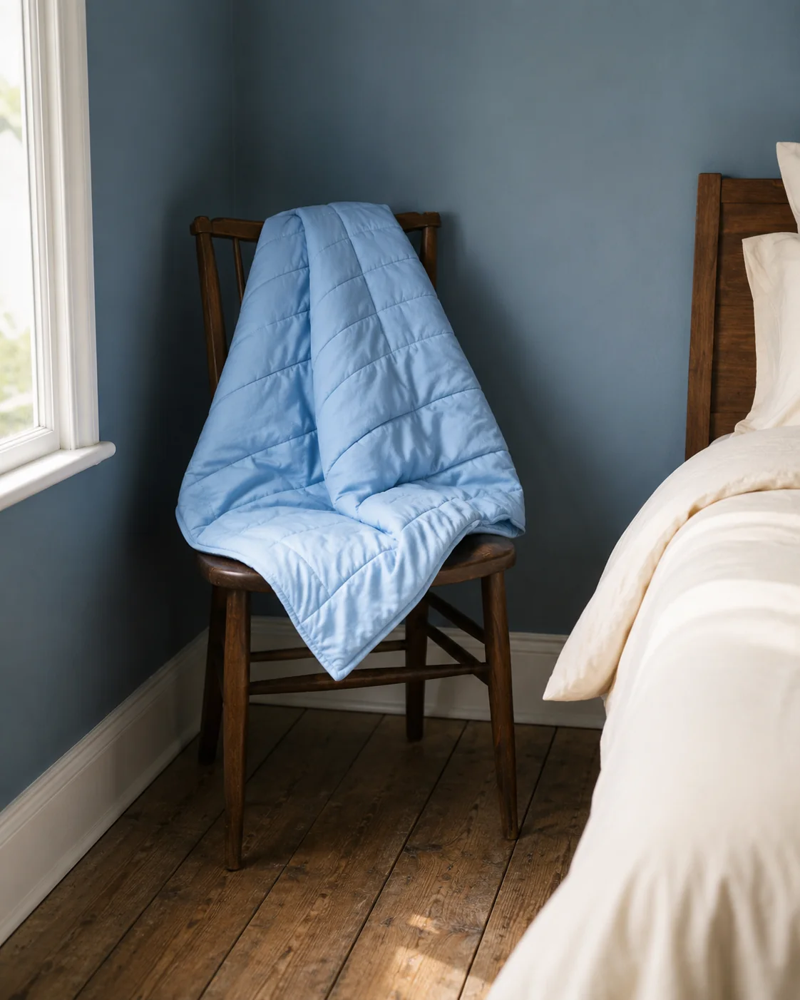 The blanket draped over a bedroom chair in the corner of the room in the morning.